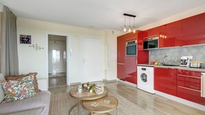 A modern kitchen with red cabinets, a washing machine, and a dining area with a sofa and coffee table. - Studio Near Beach, Sea View & Garage, Antibes, France (Antibes)