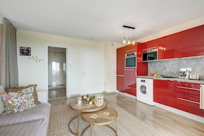 Une cuisine moderne avec des meubles rouges, un lave-linge et un coin repas comprenant un canapé et une table basse.
