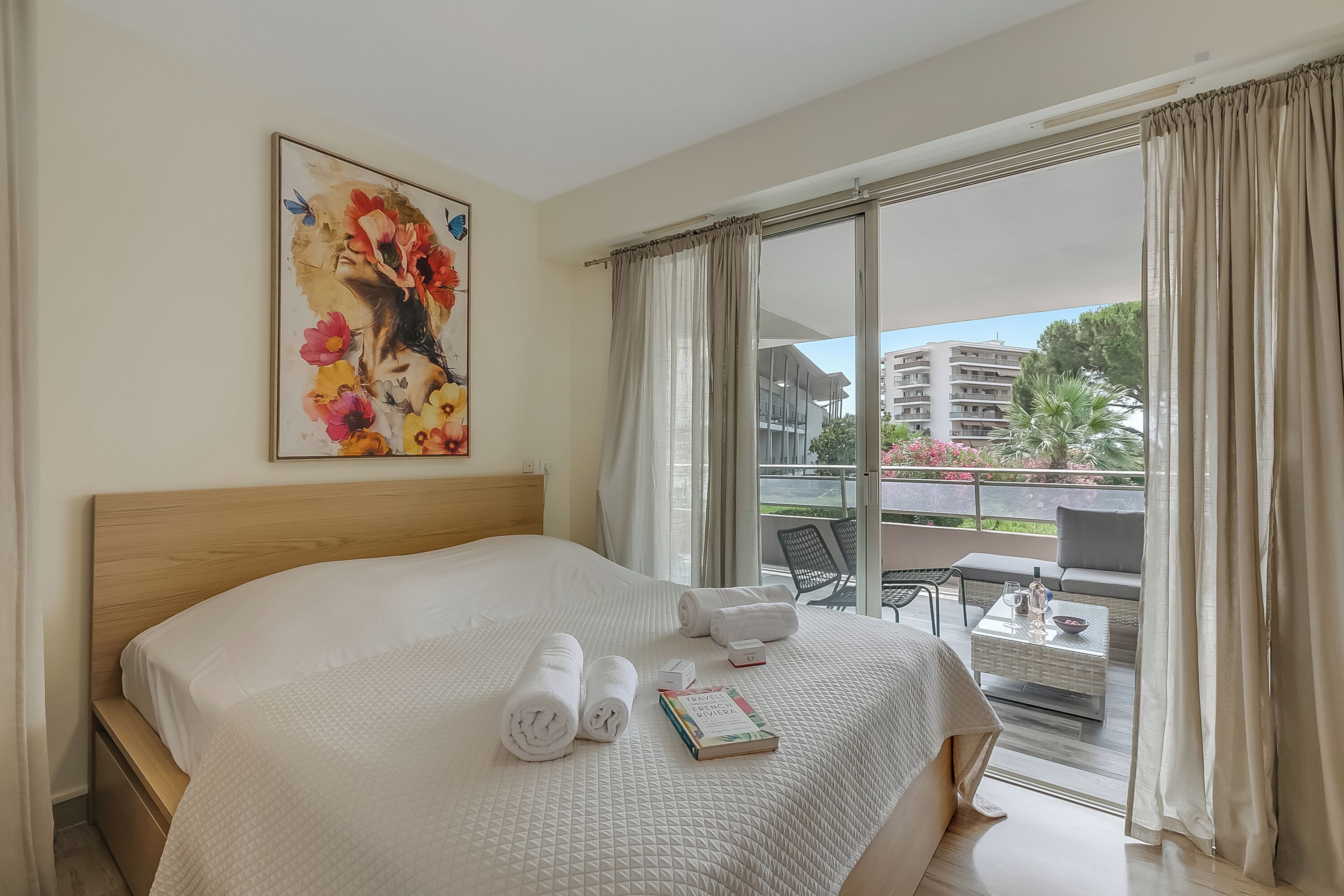 Une chambre d’hôtel avec un grand lit, un balcon doté d’une table et de chaises, et un tableau accroché au mur.