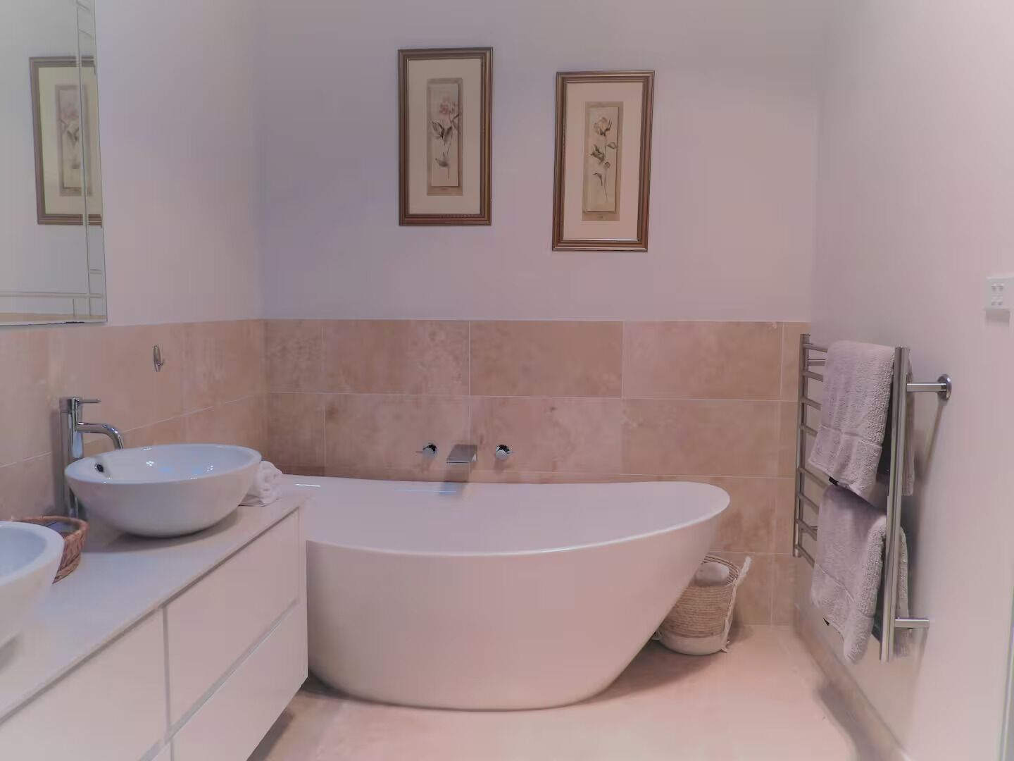 Une salle de bain moderne avec une baignoire sur pieds, un lavabo et deux œuvres d’art florales encadrées accrochées au mur.
