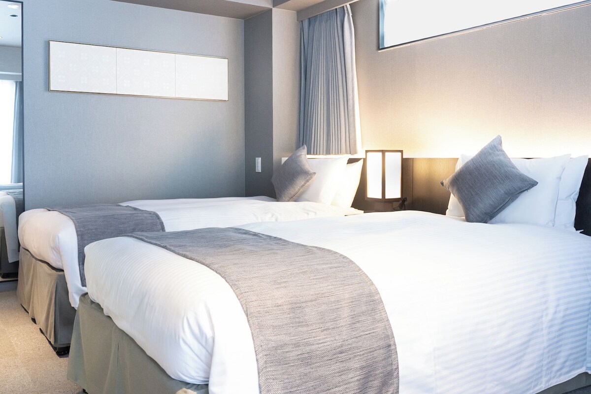 A modern hotel room with a large bed, a smaller bed, and a seating area.
