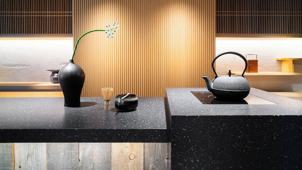 A modern reception desk with a black speckled countertop, a black vase with a green plant, a black teapot, and a small black bowl. - KIORI Hotel Higashino Toin (Kyoto)