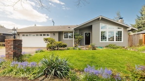 Ein Bungalow mit Garage, einer Veranda und einem gepflegten Rasen mit violetten Blumen.