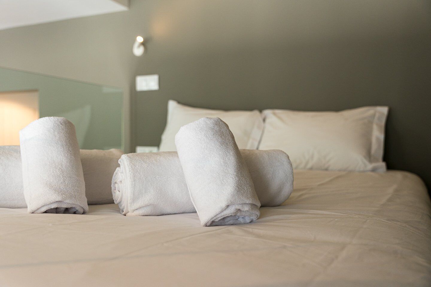 A neatly made bed with rolled towels and a lamp in the background.
