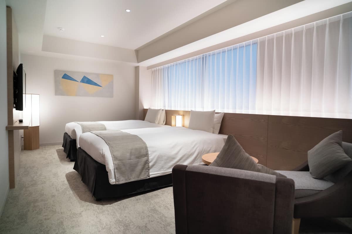 A hotel room with two beds, a sofa, a TV, and a large window with curtains.