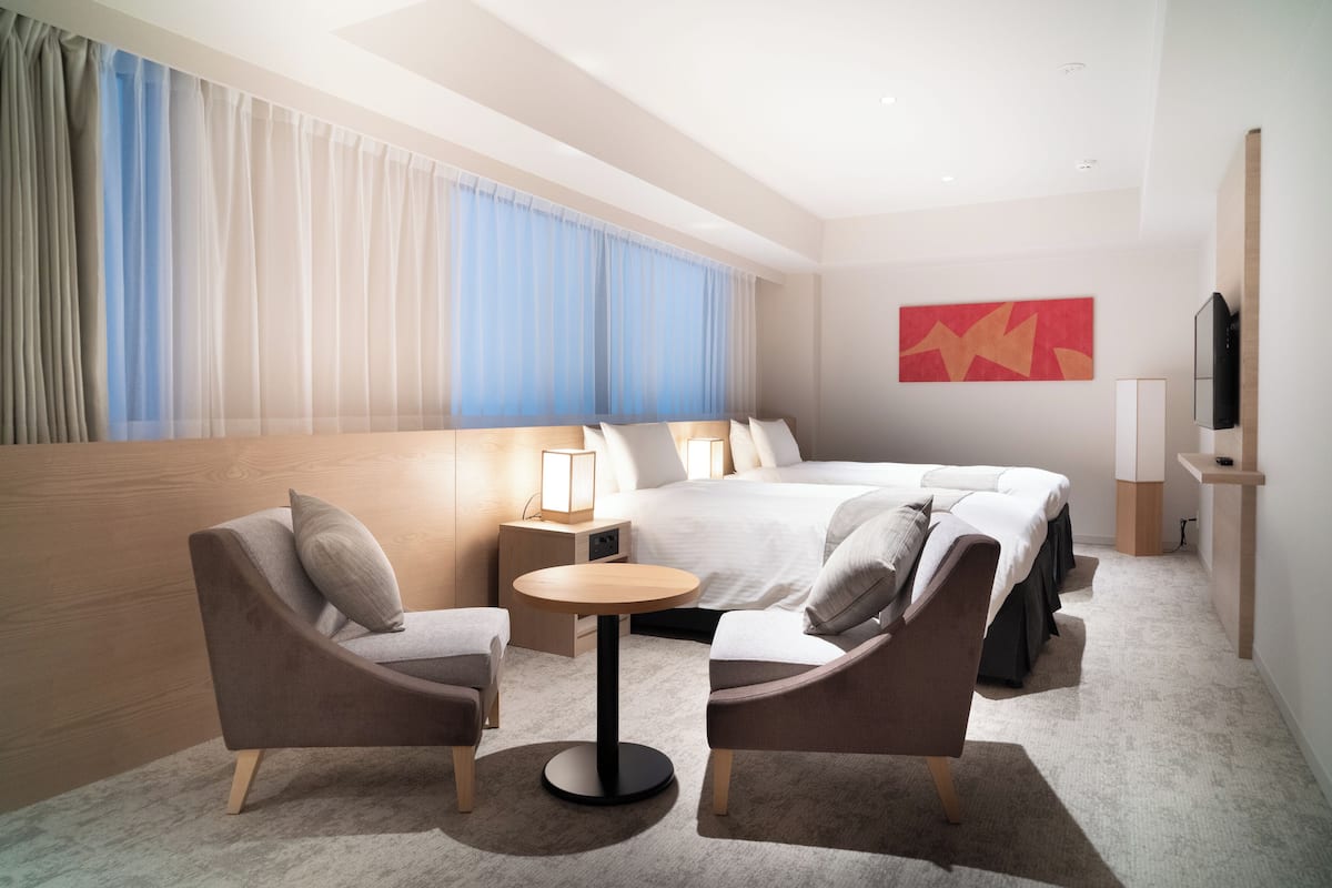 A modern hotel room with a large bed, two armchairs, a small round table, and a TV.