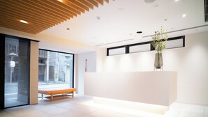A modern reception area with a bench, a reception desk, and a large window offering a view of the street. - KIORI Collection Shinmachi (Kyoto)
