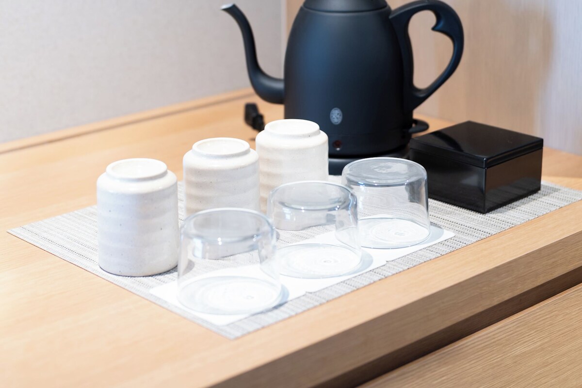A coffee station with a black coffee maker, white cups, and glasses on a wooden counter.