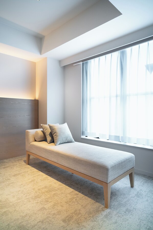 Une chambre moderne au design minimaliste, avec un canapé de couleur claire, une grande fenêtre agrémentée de rideaux légers et une palette de couleurs neutres.