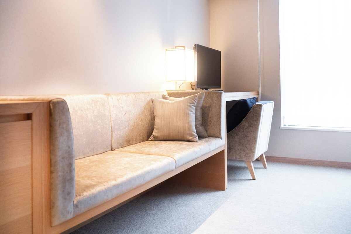 A modern, minimalist room with a sofa, a desk, and a television.