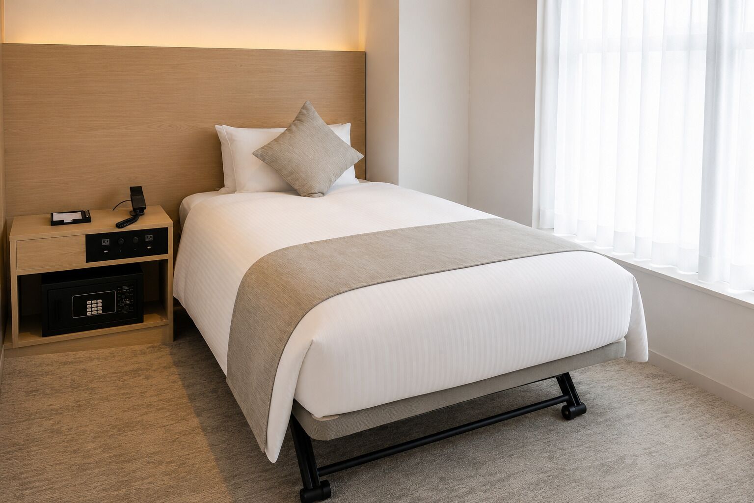 A hotel room with a bed, bedside table, and a window with curtains.