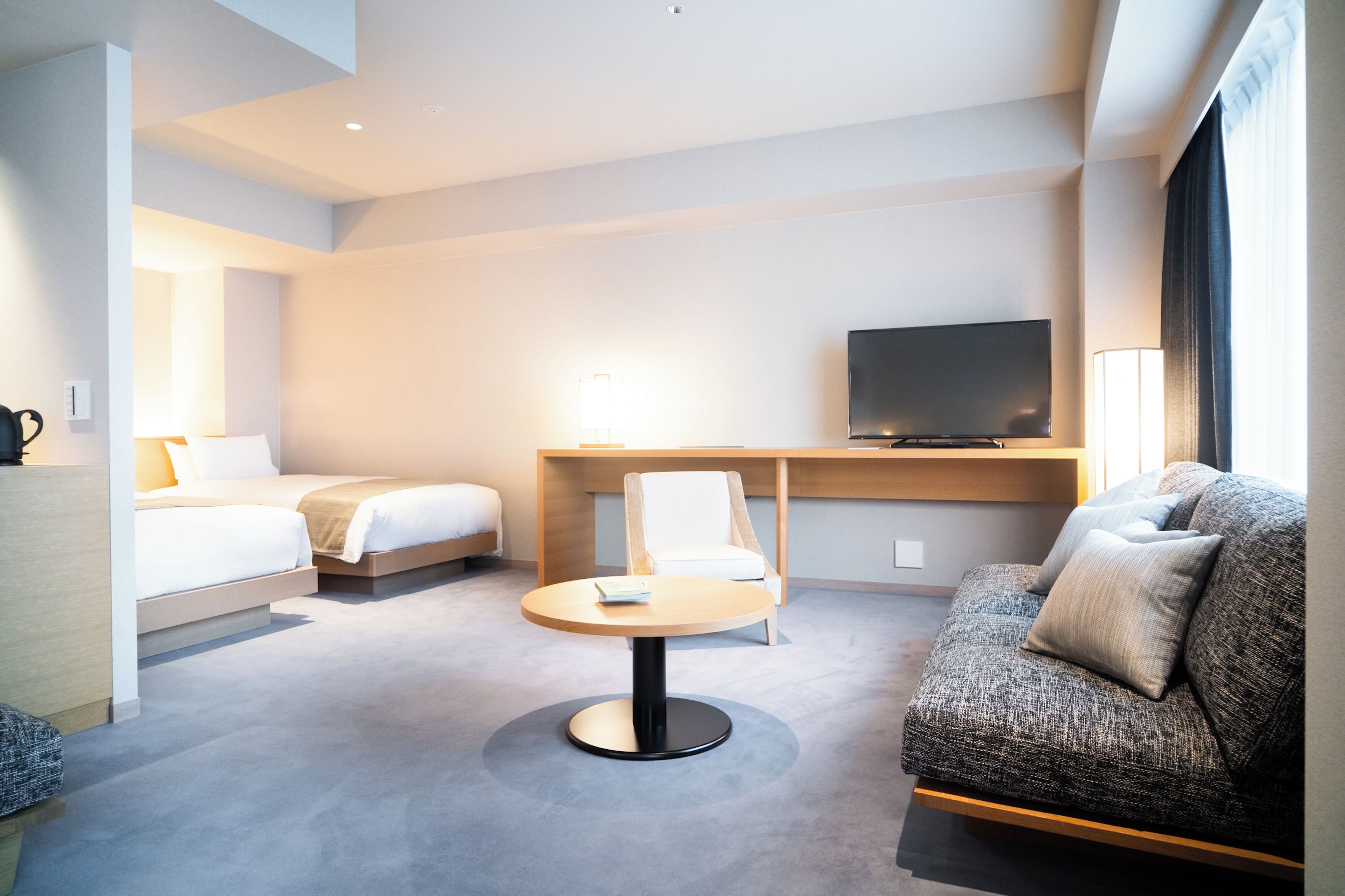 Una camera d'albergo moderna con un letto, un divano, una scrivania e una televisione a schermo piatto, e un tavolino rotondo.