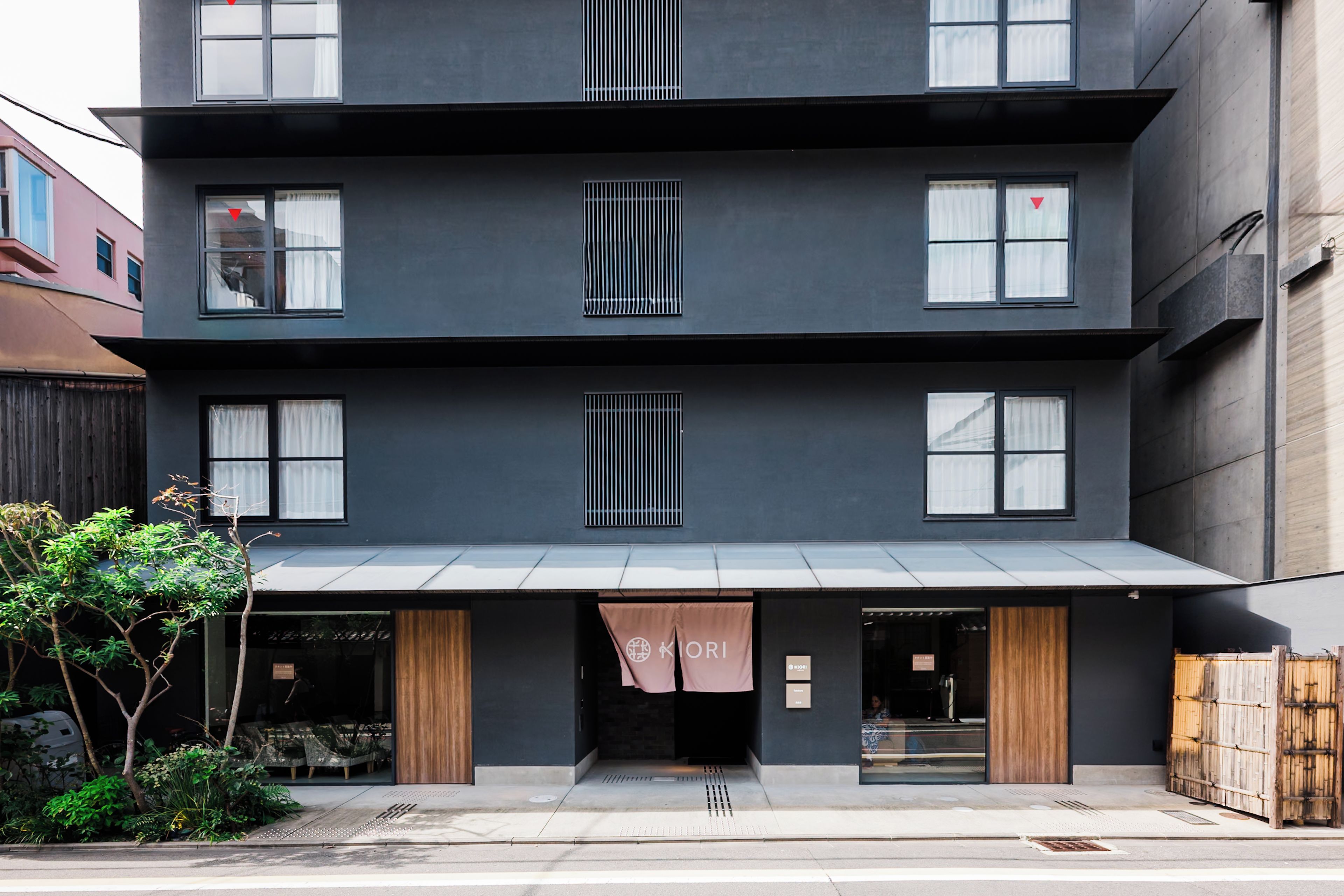 Un edificio moderno de varios pisos con fachada plana, amplias ventanas y un área de acceso cubierta.