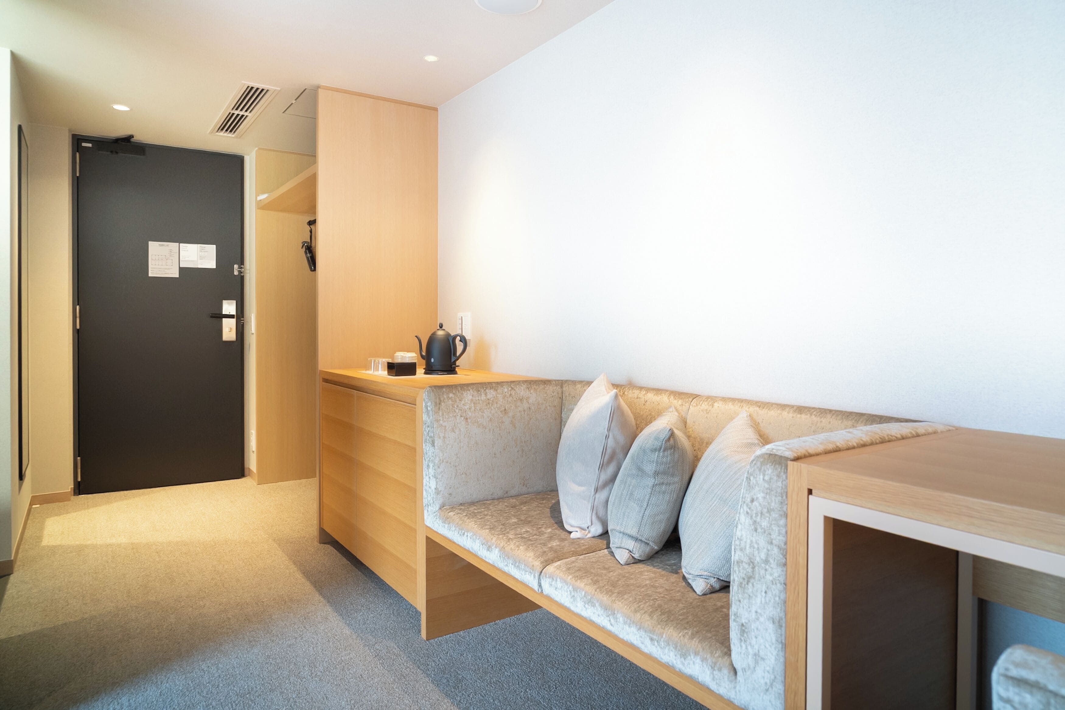 A modern, minimalist room with a built-in sofa, a wooden desk, and a dark door.