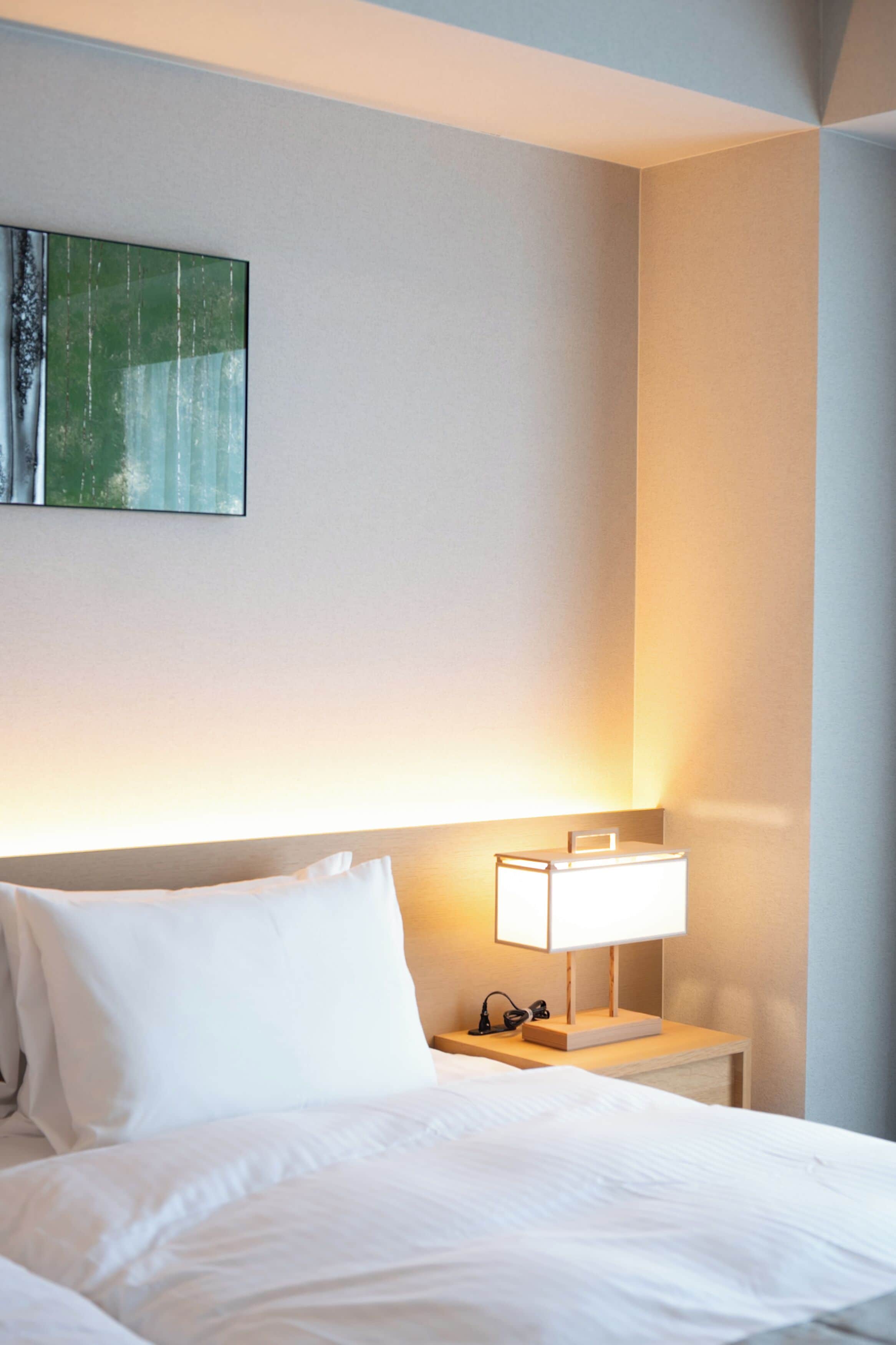 A hotel room with a neatly made bed, a bedside lamp, and a painting on the wall.