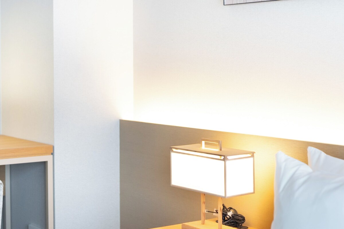 A hotel room with a neatly made bed, a bedside table with a lamp, and a wall-mounted artwork.