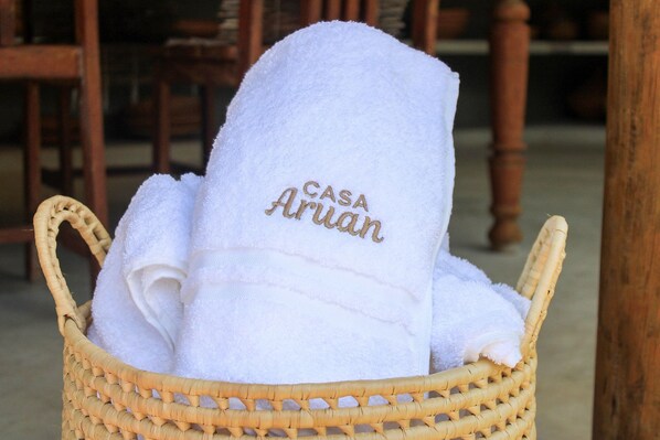 A wicker basket containing a white towel with "CASA Aruan" embroidered on it.
