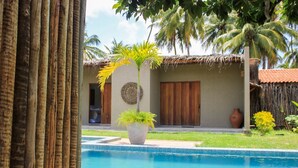 A pool area with a palm tree planter, a thatched-roof building, and a large vase.