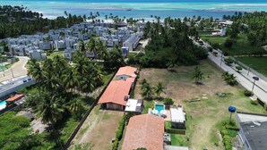 An aerial view of a coastal residential area with modern buildings, a central open space, and a view of the ocean.
