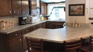 A kitchen with dark wooden cabinets, a granite countertop, a built-in microwave, and a large island with chairs.
