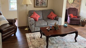 A living room with a grey sofa, a brown leather armchair, a wooden coffee table, and a floor lamp.