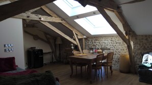 A cozy attic room with a skylight, wooden beams, a dining table, and a stone wall. - Master bedroom 50 m2 Great comfort 5 minutes from Lac de Neufond (Vergt)