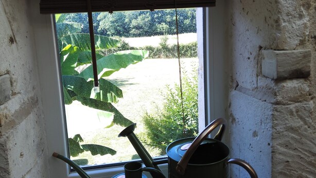 A rustic room with a window overlooking a garden, wooden beams on the ceiling, and two metal pots on the windowsill. - Master bedroom 50 m2 Great comfort 5 minutes from Lac de Neufond (Vergt)