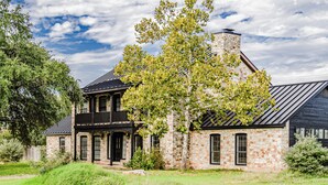 A two-story stone house with a black roof, a large tree in front, and a clear sky. - The House of Proverbs-All about our Heavenly Father, Family and Good Fellowship! (Round Rock)