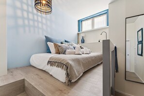 Een slaapkamer met een bed, een raam, een nachtkastje en een spiegel.