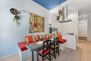 Een knus leefruimte met een eethoek, kitchenette en een kleurrijk abstract schilderij.