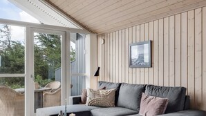 Un salon moderne avec un canapé gris, une table basse ronde agrémentée d’un plateau et d’une bougie, et une grande fenêtre donnant sur un paysage verdoyant.