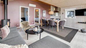Un salon chaleureux avec une cheminée, un canapé, une table basse et un coin repas comprenant des chaises et une table.