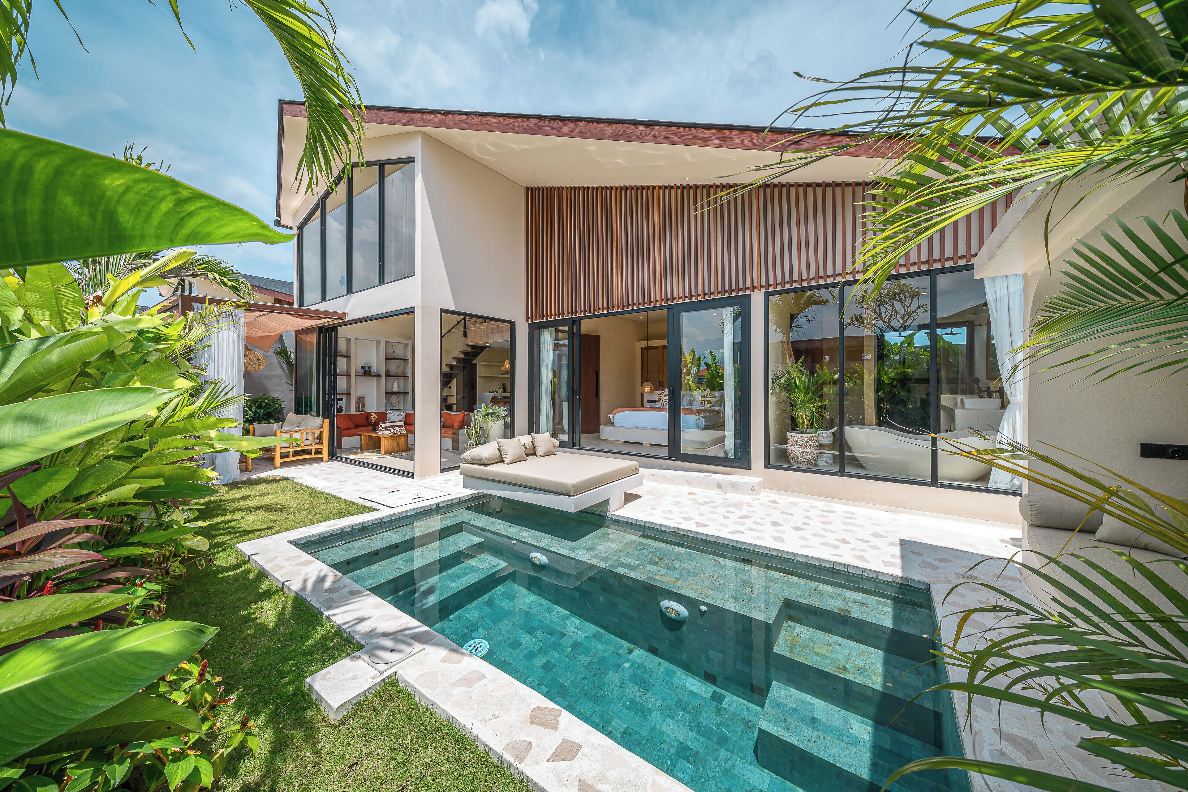 Una casa moderna con piscina, mobiliario exterior y abundante vegetación.