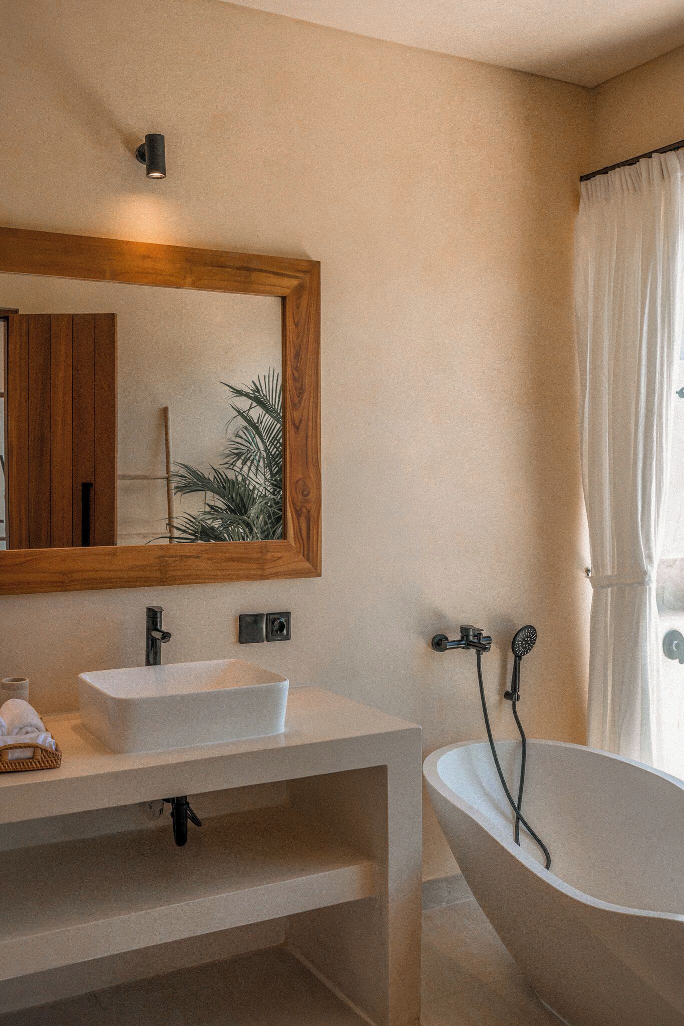 Un baño con una bañera independiente, un espejo con marco de madera y un lavabo blanco.