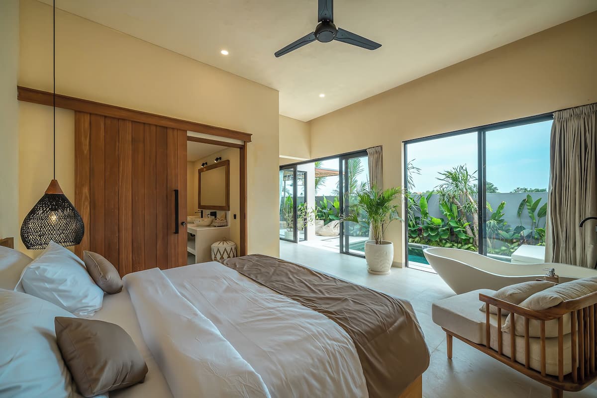 A modern bedroom with a large bed, a sitting area, a bathtub, and a view of the outdoors.
