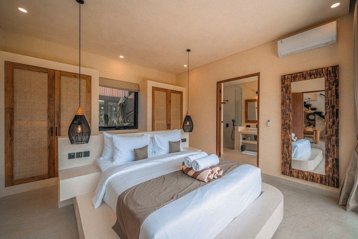 A modern hotel room with a large bed, a bathroom with a mirror, and a shower area.