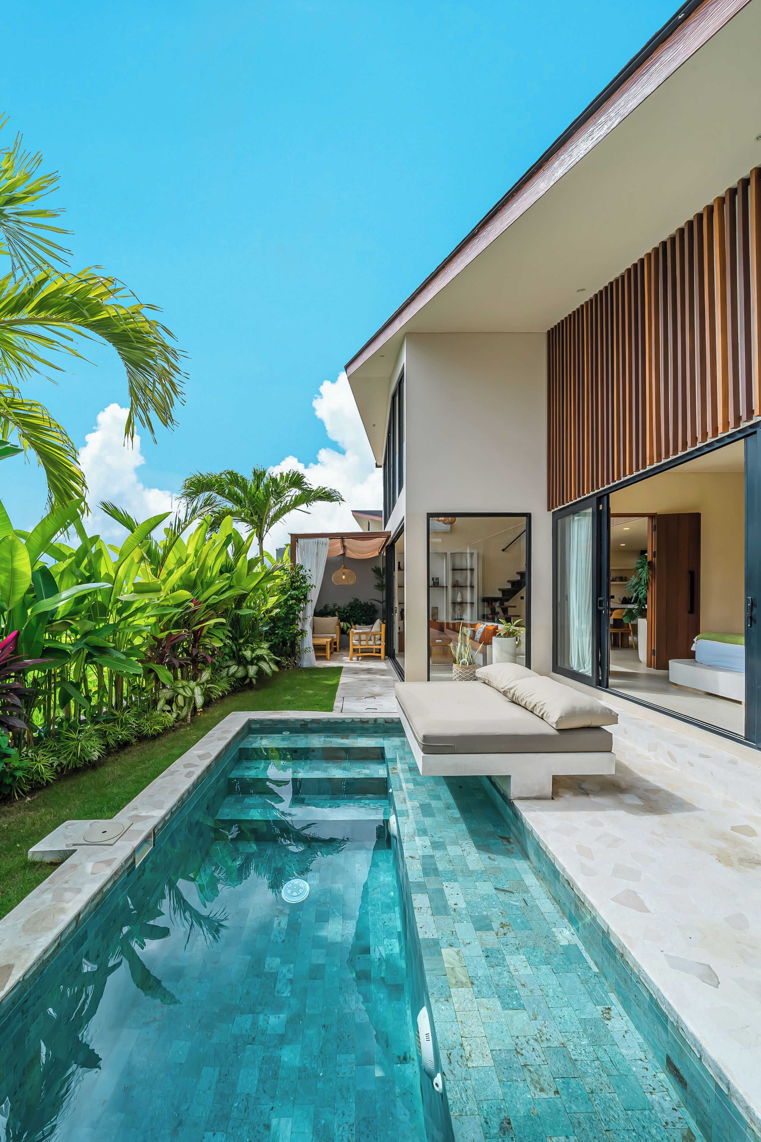 A modern house with a swimming pool, a well-maintained garden, and a large sliding glass door leading to a living area.