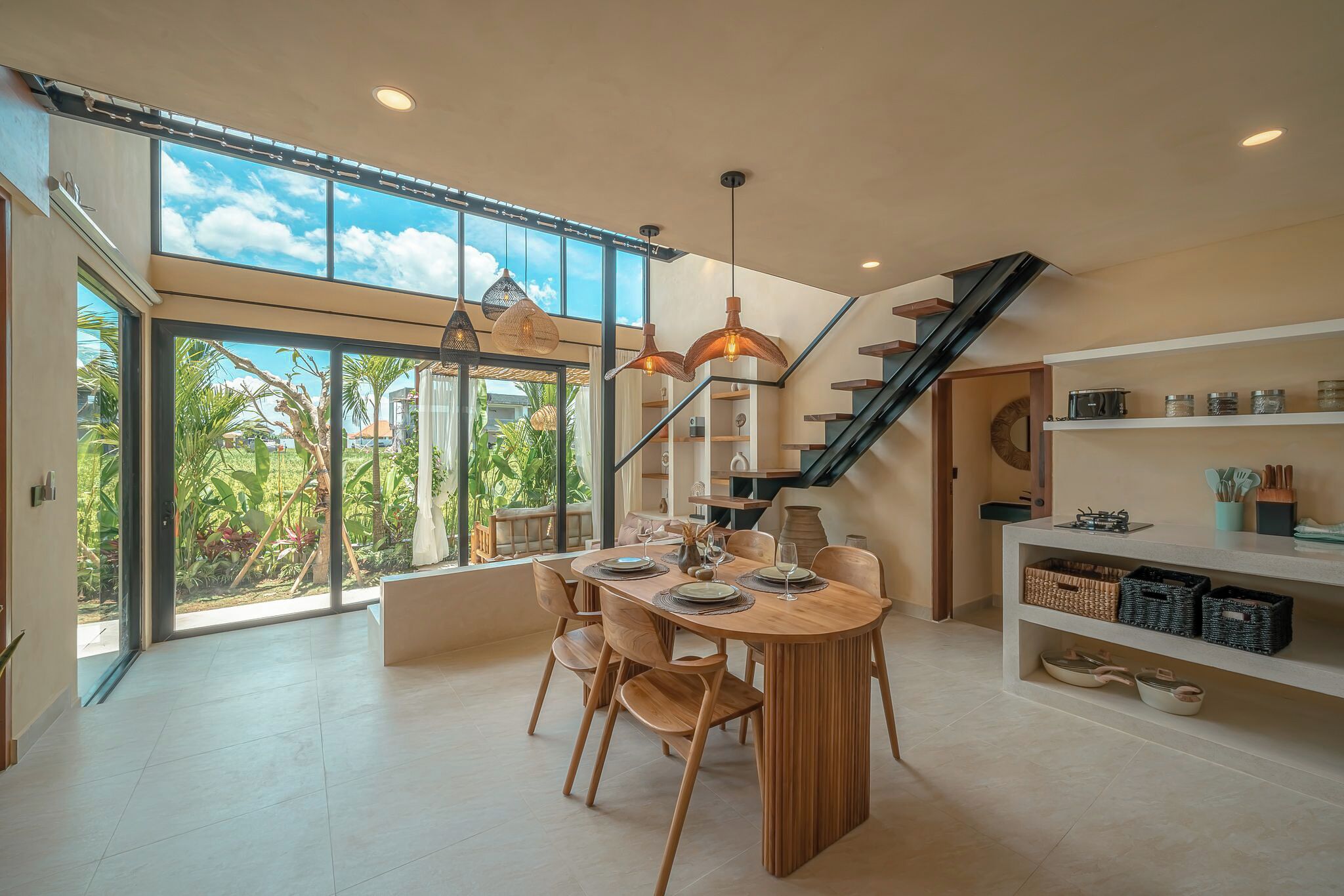Una cocina moderna con una isla grande, una zona de comedor con una mesa y sillas de madera, y una escalera que sube a un nivel superior.