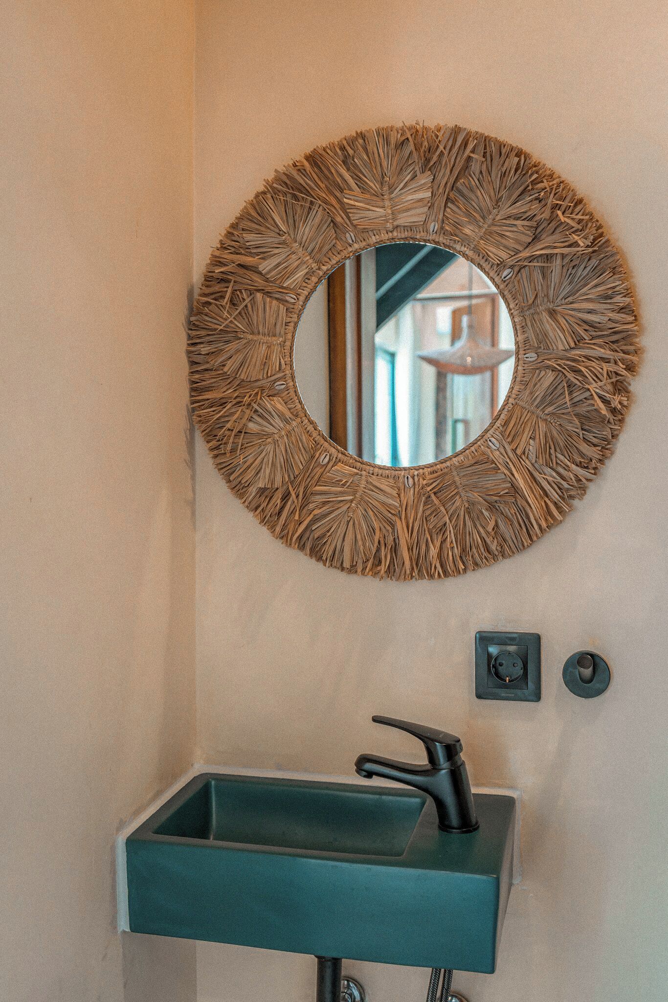 A bathroom with a round mirror with a natural leaf design, a teal sink, and a black faucet.
