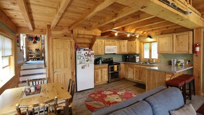 Interior de una cabaña de madera con cocina, comedor y sofá.