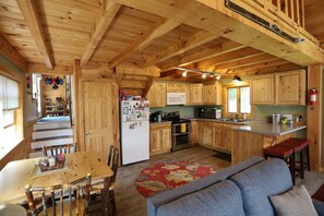 A wooden cabin interior with a kitchen, dining area, and a sofa.
