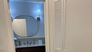 A narrow hallway with a wooden floor, a patterned rug, a bathroom with a white vanity, a mirror, and a wall-mounted lamp. - Charming Quiet 1-bedroom 1 bath ADU with AC, WiFi in Savannah (Savannah)