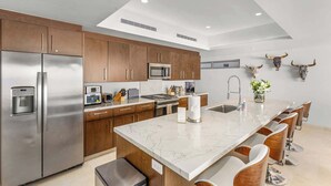 A modern kitchen with stainless steel appliances, wooden cabinets, a marble countertop, and a bar area with bar stools. - Oceanview Pedregal Condo: Jacuzzi, Balcony & (Cabo San Lucas)