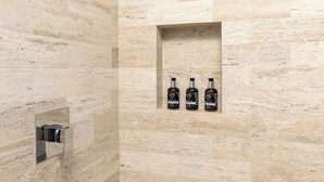 A bathroom with a stone wall, a built-in shelf with three bottles, and a mirror. - Oceanview Pedregal Condo: Jacuzzi, Balcony & (Cabo San Lucas)