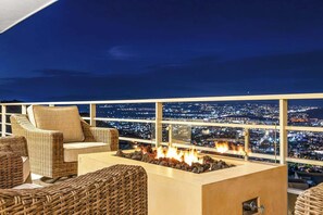 A rooftop terrace with wicker furniture, a fire pit, and a city view at night. - Oceanview Pedregal Condo: Jacuzzi, Balcony & (Cabo San Lucas)