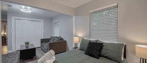 Un dormitorio moderno con una cama, un sofá, una mesita y una ventana con persianas.
