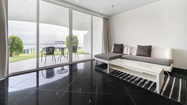 Un salon moderne doté d’une porte-fenêtre coulissante donnant sur un balcon, d’un canapé blanc, d’une table basse en verre et d’un tapis rayé noir et blanc.