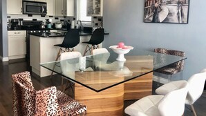 Une cuisine moderne avec des meubles blancs, un four à micro-ondes et un coin repas comprenant une table et des chaises en verre.