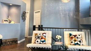 Un salon moderne avec un mur d’accent bleu, un canapé blanc agrémenté de coussins à motifs et un lustre.