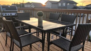Une terrasse avec une table rectangulaire et six chaises en osier, un arrangement décoratif composé de cactus et un barbecue.